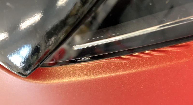 Schwarze Folie wirft sich am Rand eines Scheinwerfers zu Rümpfen auf — typischer Fehler beim Überfolieren: die Folie wurde zu weit hinter das Anbauteil geklebt und quetscht beim Wiederaufsetzen heraus.