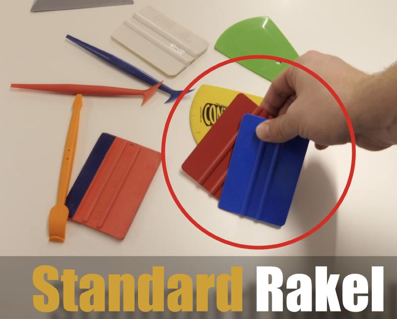 Verschiedene Wrapping-Rakel auf einer Werkbank — weicher blauer und harter roter Standard-Rakel in der Hand, daneben Stechfinger-Rakel, Klapp-Rakel und Mulden-Werkzeug